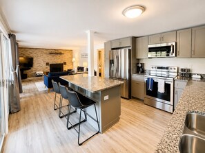 A modern kitchen with stainless steel appliances, a granite countertop, and a bar area with stools.