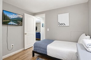 A bedroom with a bed, a TV, a door leading to another room, and a wall with a sign.