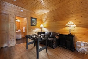 Um quarto aconchegante com mesa de pebolim, sofá e ventilador.