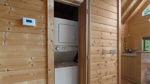 A wooden interior with a laundry area featuring a washing machine and dryer, a small window, and a wooden cabinet. - Secluded Mountain Cabin with Hot Tub, Fire Pit, Games and Views (Sevierville)
