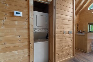 Ein Holzinnenraum mit einer Waschküche, die eine Waschmaschine und einen Trockner, ein kleines Fenster und einen Holzschrank beinhaltet.