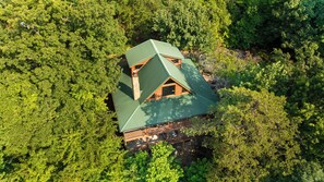 An aerial view of a cabin with a green roof, surrounded by dense forest. - Secluded Mountain Cabin with Hot Tub, Fire Pit, Games and Views (Sevierville)