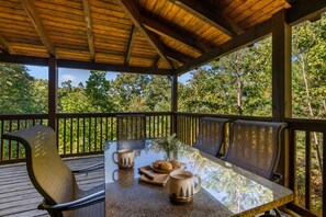 An outdoor wooden deck with a glass-top table, two chairs, and a mug with a forest design. - Secluded Mountain Cabin with Hot Tub, Fire Pit, Games and Views (Sevierville)
