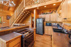 L’intérieur d’une cabane en bois comprend une cuisine, un réfrigérateur, une cuisinière et un escalier menant à une mezzanine.