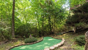 A green artificial golf course surrounded by dense trees and a stone wall. - Secluded Mountain Cabin with Hot Tub, Fire Pit, Games and Views (Sevierville)