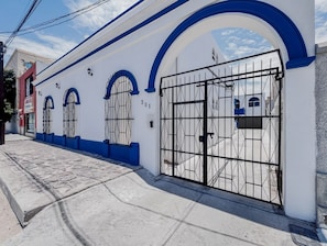A building with a white facade and blue accents, featuring a large metal gate and arched windows. - La Ventana Housing cerca del malecon (La Paz)