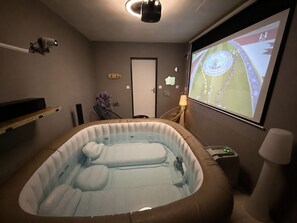 A room with a hot tub, a projector screen displaying a sports event, and a door with a decorative item. - Smart home, EV charging station, air-conditioned, near Cognac, sleeps 6 (Châteaubernard)