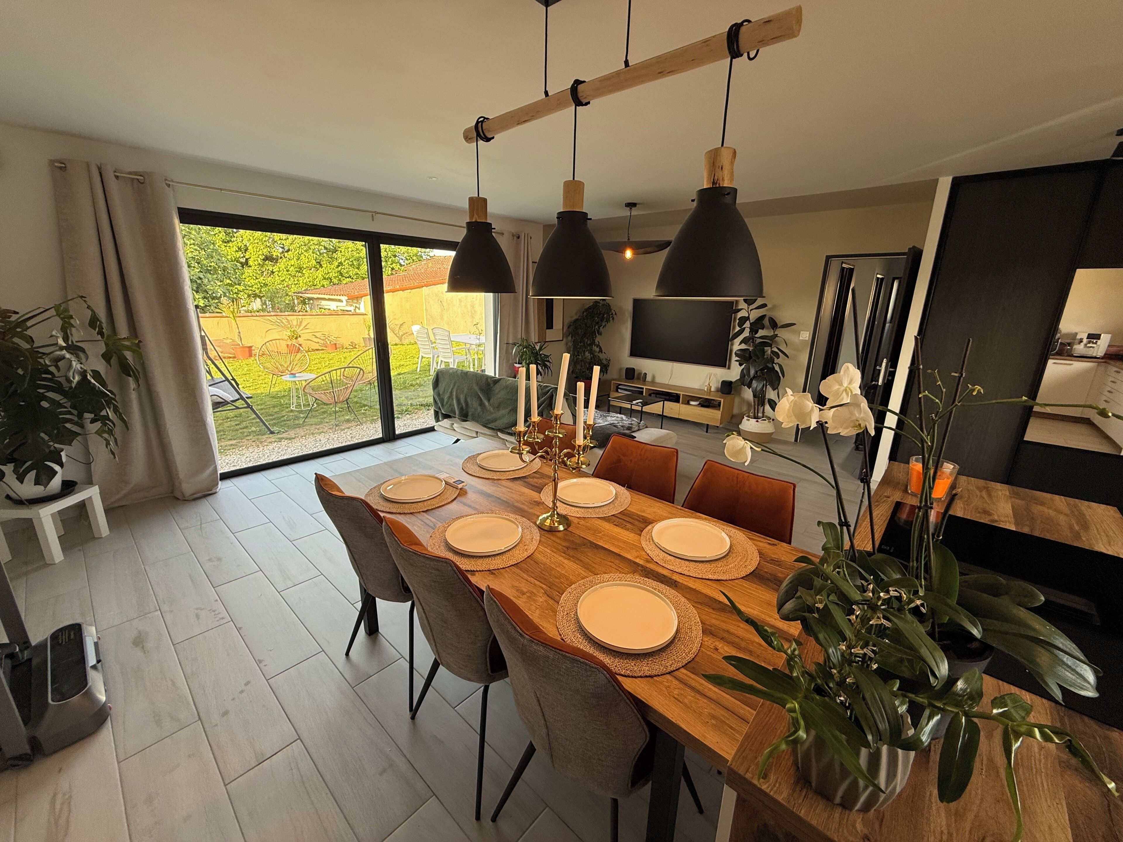 A dining area with a wooden table set for four, surrounded by chairs, with a large window offering a view of the outdoors.