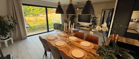 A dining area with a wooden table set for four, surrounded by chairs, with a large window offering a view of the outdoors.