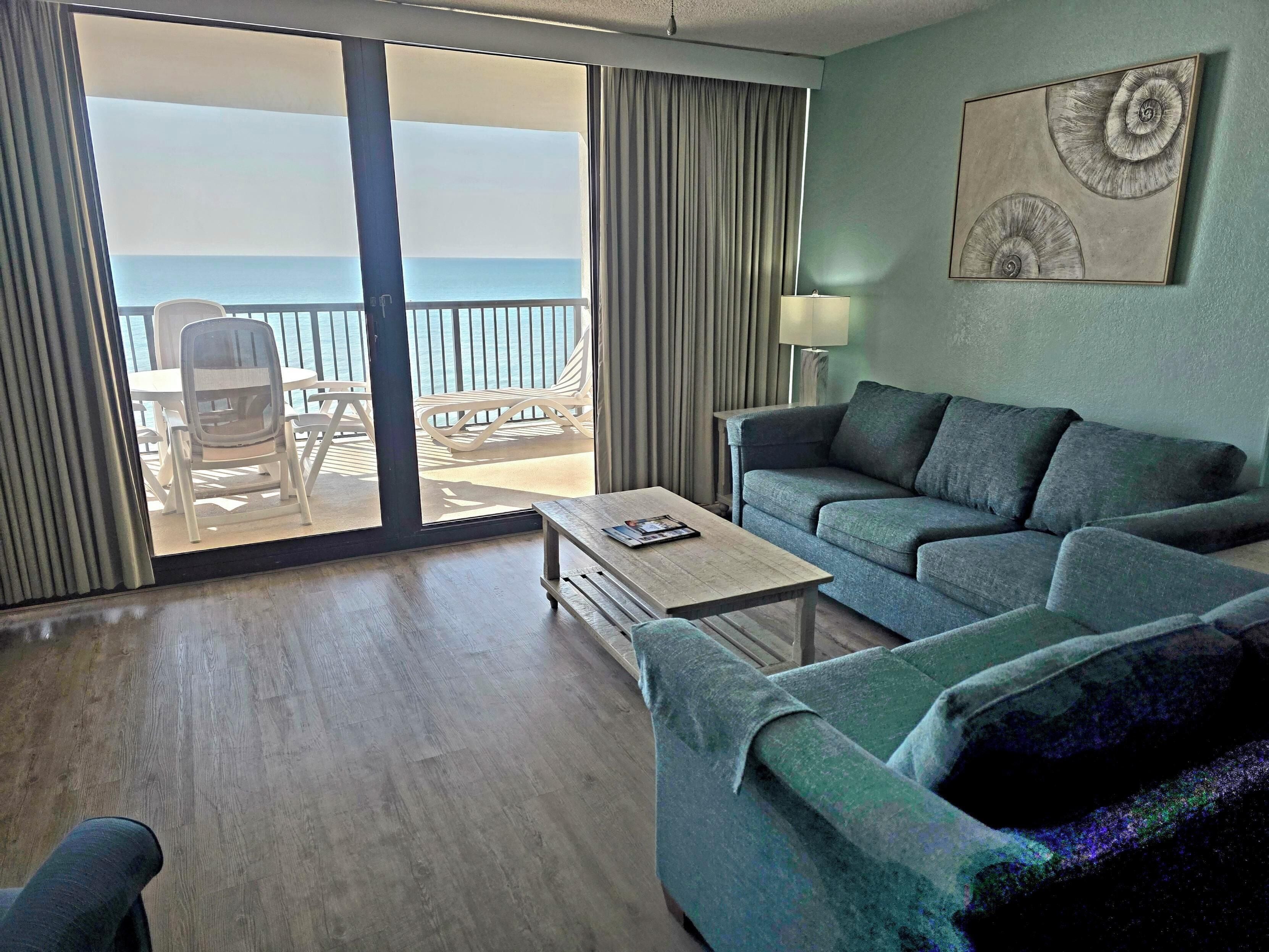 A room with a sofa, a coffee table, and a view of the ocean through a sliding door.