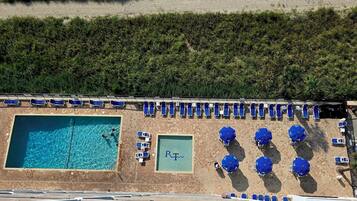 A rooftop pool area with multiple sun loungers and umbrellas, surrounded by greenery.
