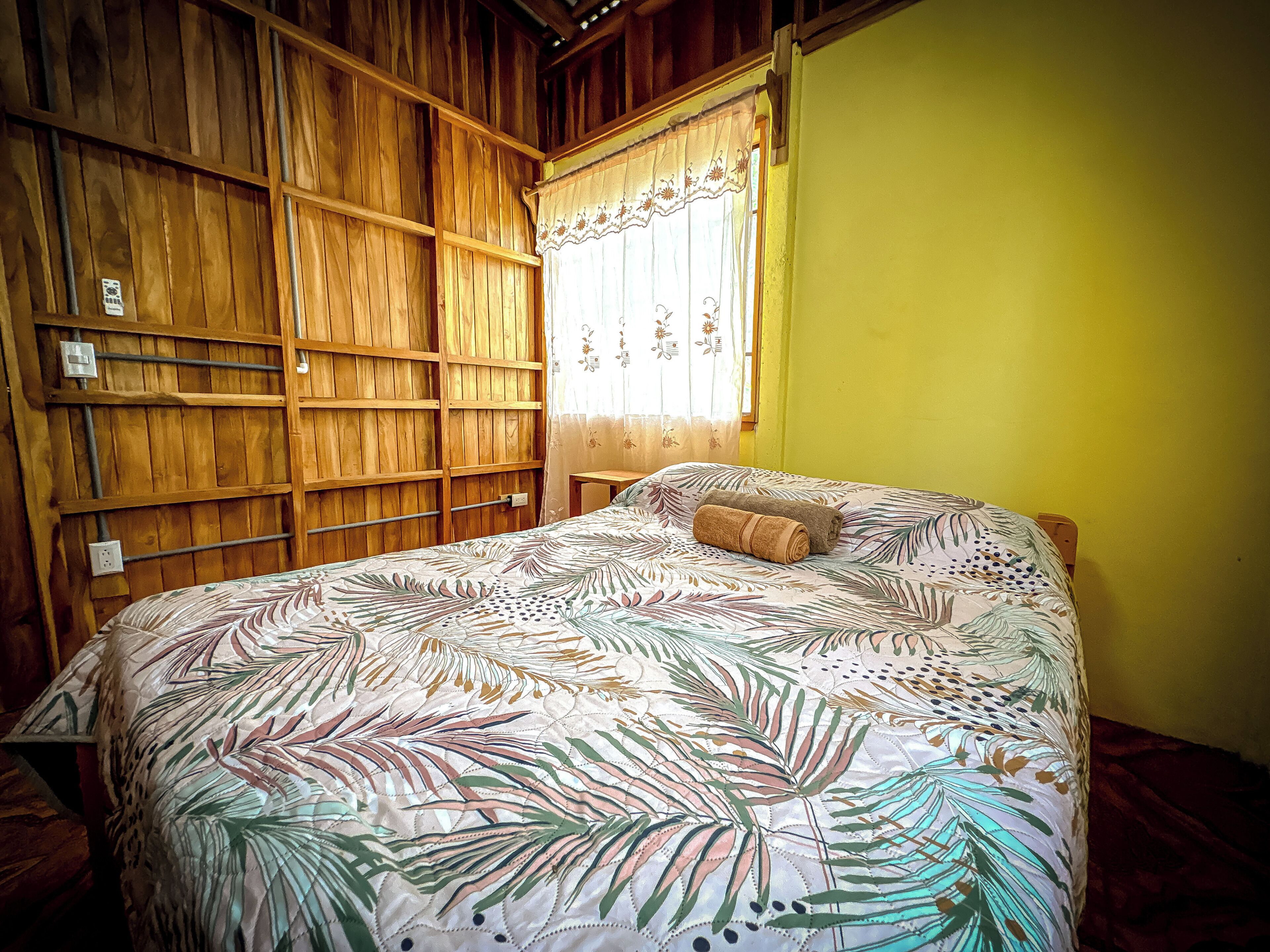Ein Zimmer mit einem Bett, Holzvertäfelung, einem Fenster mit Vorhängen und einer gelben Wand.