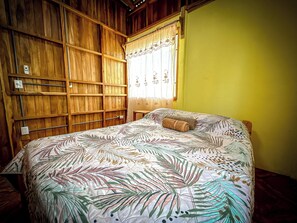 A room with a bed, wooden paneling, a window with curtains, and a yellow wall.