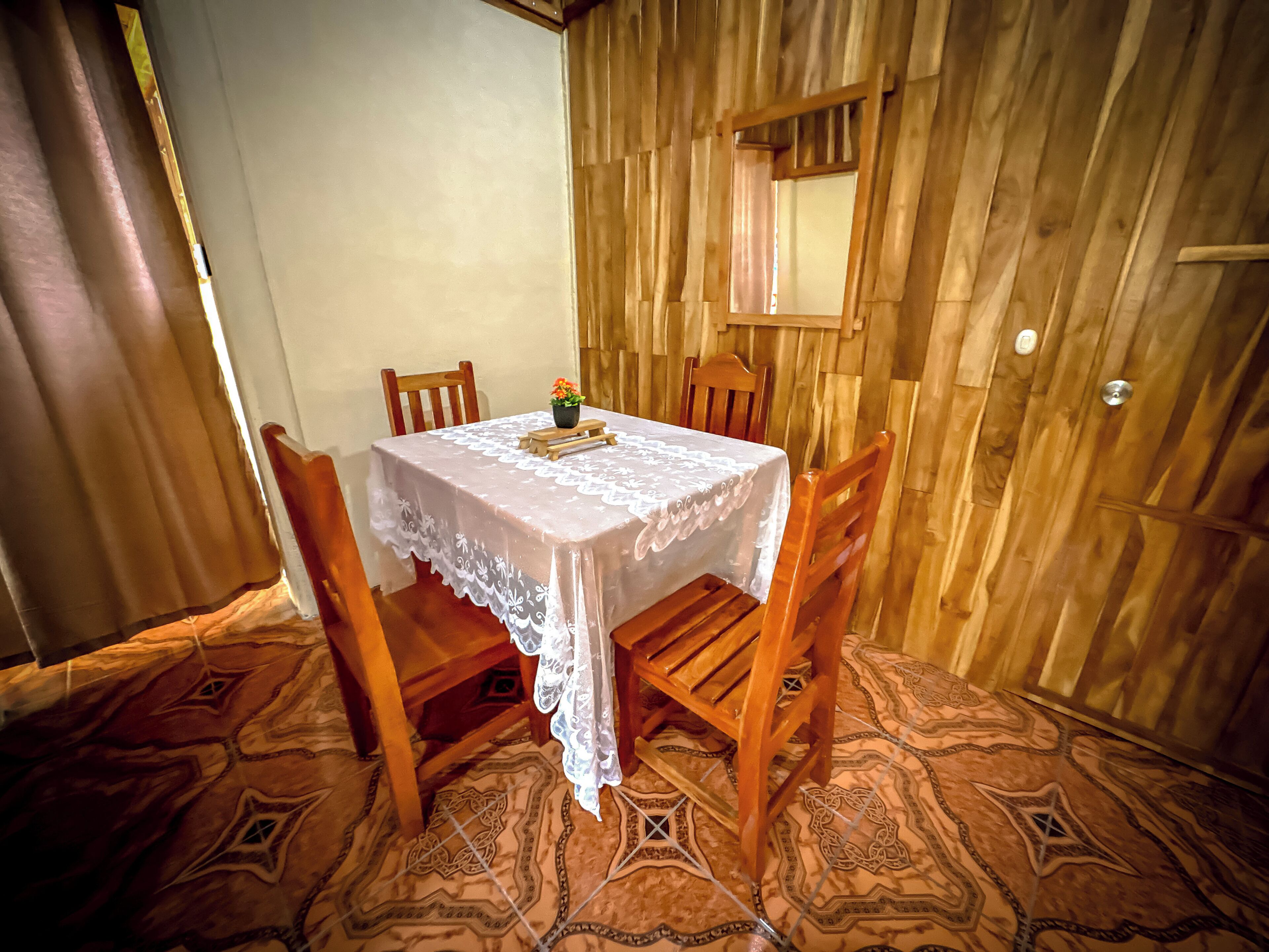 Ein Essbereich mit einem Tisch, der mit einer weißen Tischdecke bedeckt ist, Holzsesseln und einer Topfpflanze.