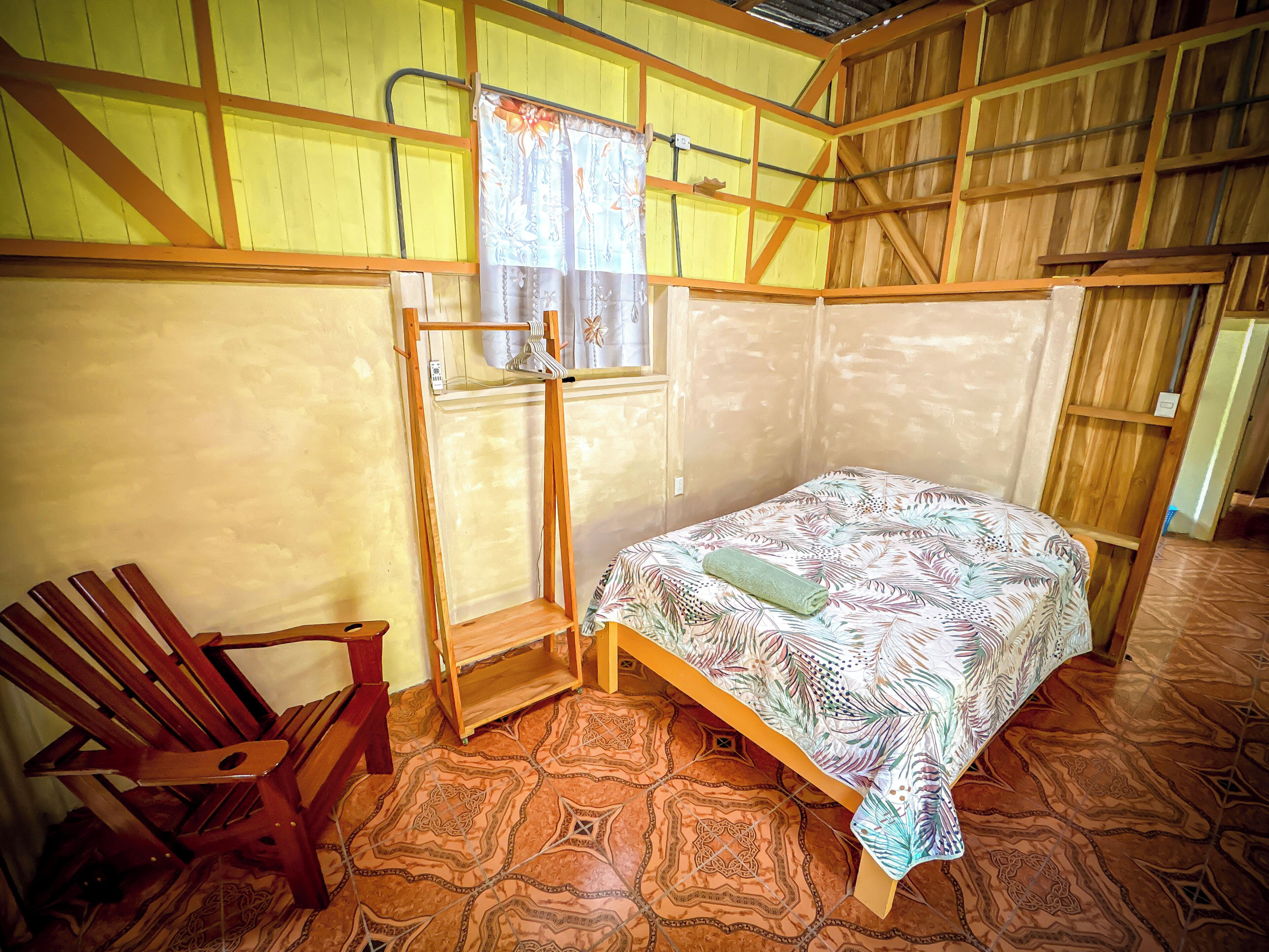 Una habitación con cama, una silla de madera, un perchero y suelo estampado.