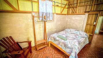 Una habitación con cama, una silla de madera, un perchero y suelo estampado.