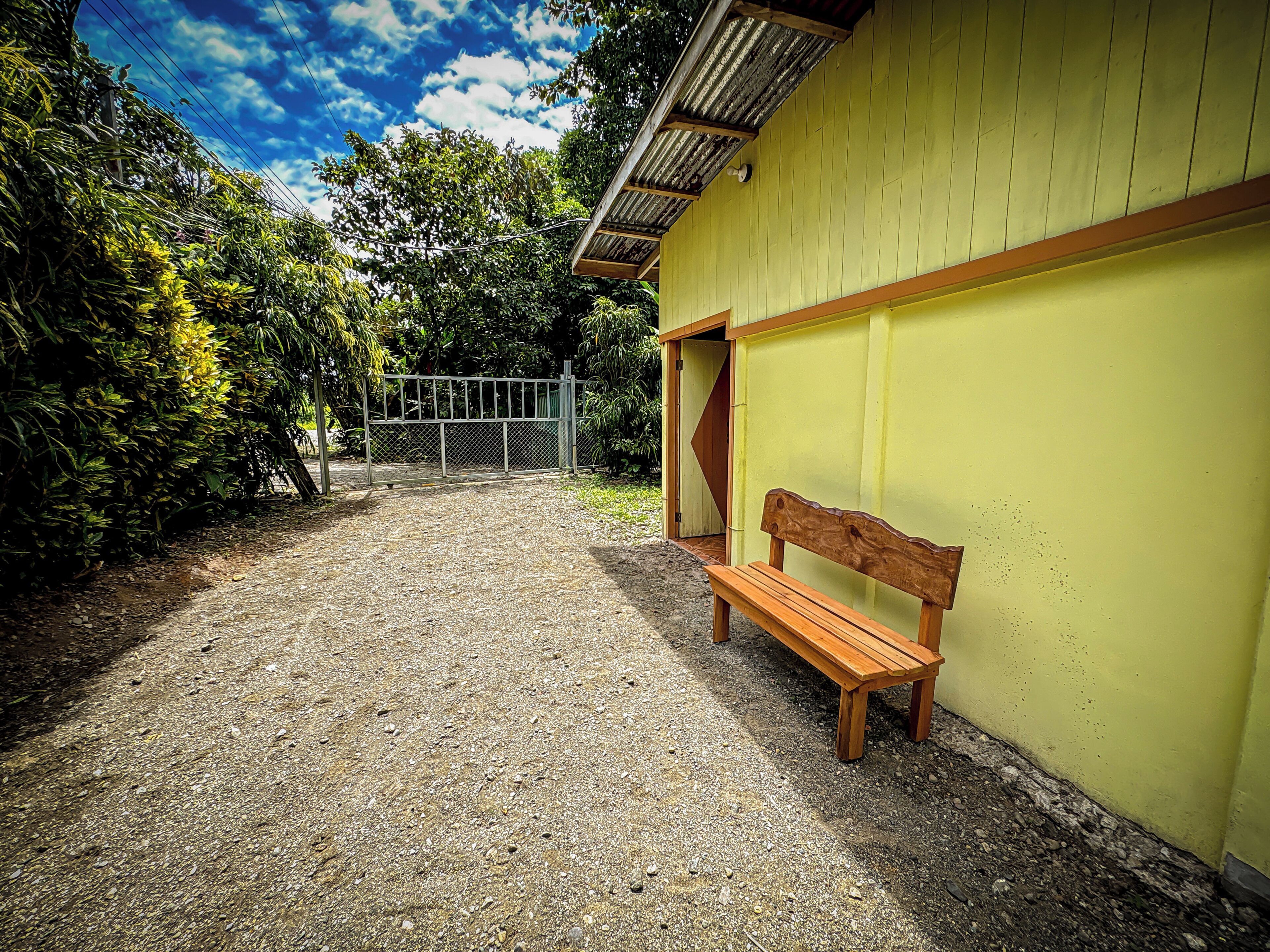 A gravel path leading to a yellow building with a wooden bench.