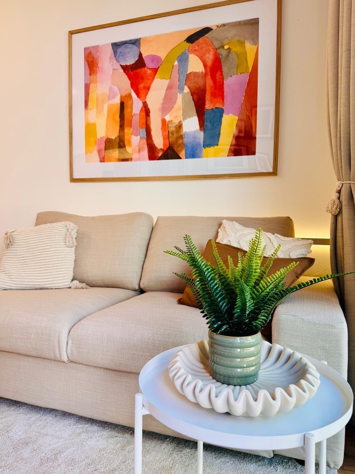 A living room with a beige sofa, a white coffee table, and a framed abstract painting on the wall.