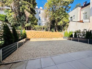 A courtyard with a gravel area, a wooden bench, and a metal fence. - Vienna Garden Suites | Imperial | Terrace & Air Conditioning (Wien)