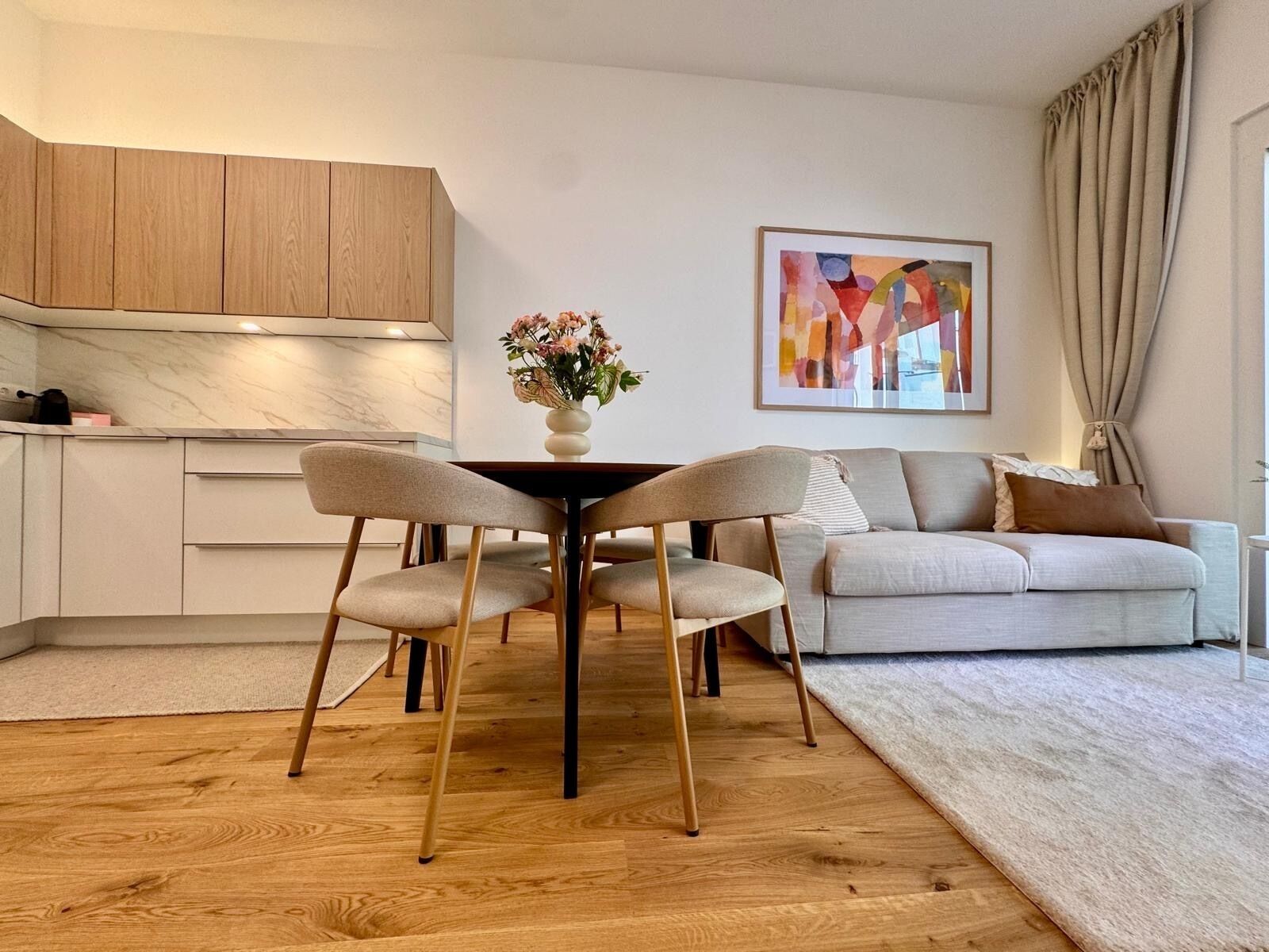 A modern living space with a dining table, chairs, a sofa, and a kitchen area.