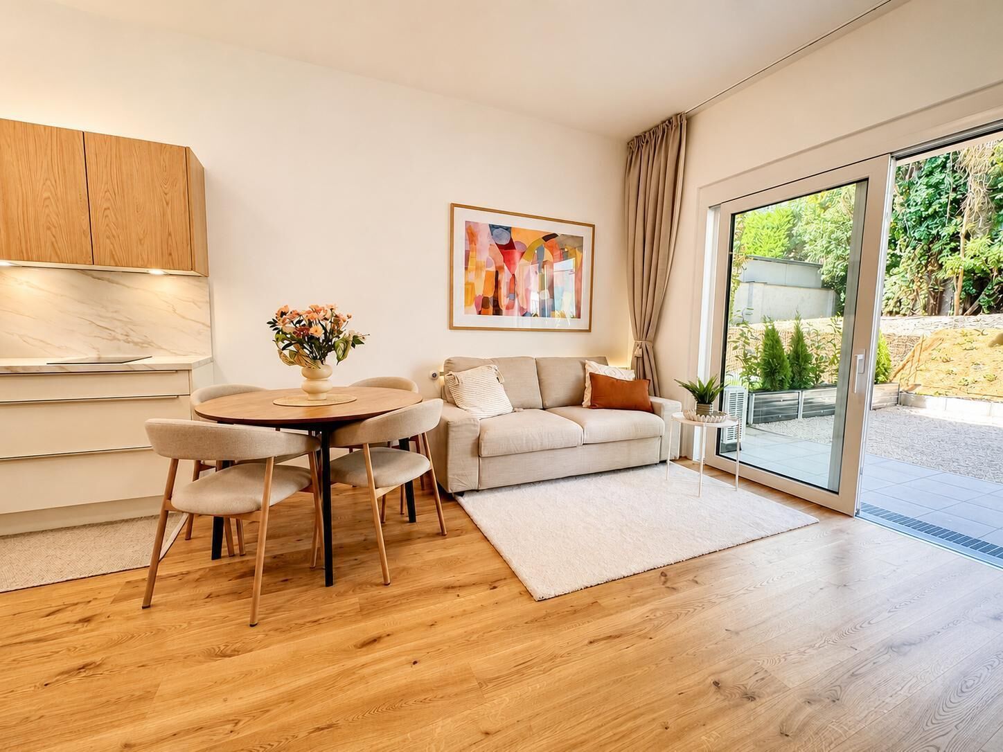 A modern living room with a round dining table, a sofa, and a large sliding glass door leading to an outdoor area.