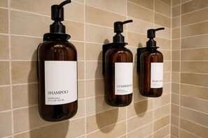 Tres ampolles de xampú i condicionador damunt d'una paret de rajola.