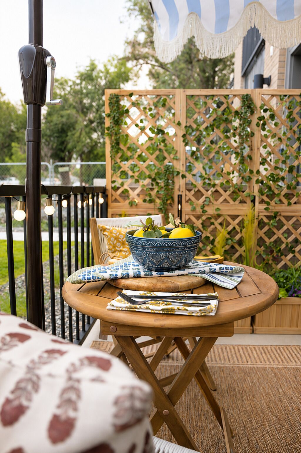 An outdoor seating area with a round wooden table, a bowl of fruit, and a patterned tablecloth.