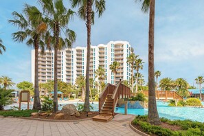 A resort with a swimming pool, palm trees, and a multi-story building with balconies. - Ocean View, 8th Floor Condo! No Hidden Fees! (Destin)