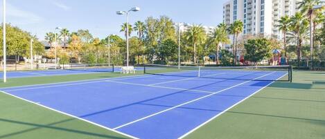 A tennis court with a net, surrounded by trees and buildings.