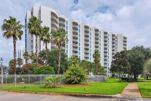 A multi-story hotel with balconies, surrounded by palm trees and a white fence. - Ocean View, 8th Floor Condo! No Hidden Fees! (Destin)