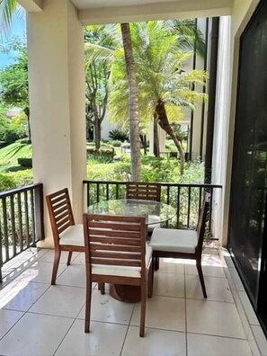 Ein Balkon mit Glastisch und Stühlen, umgeben von einer Brüstung, mit Blick auf Grünflächen und Palmen.