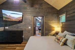 Ein Schlafzimmer mit einem großen Bett, einem an der Wand montierten Fernseher, Holzwänden und Blick in den Essbereich.