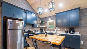 A modern kitchen with dark blue cabinets, stainless steel appliances, and a wooden island with chairs. - Theater! Sauna! Jacuzzi! Firepit! EV Charger (Cosby)