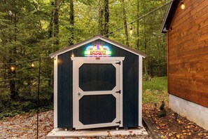 A small, dark-colored shed with a neon sign reading 'THEATER' on top, surrounded by trees. - Theater! Sauna! Jacuzzi! Firepit! EV Charger (Cosby)