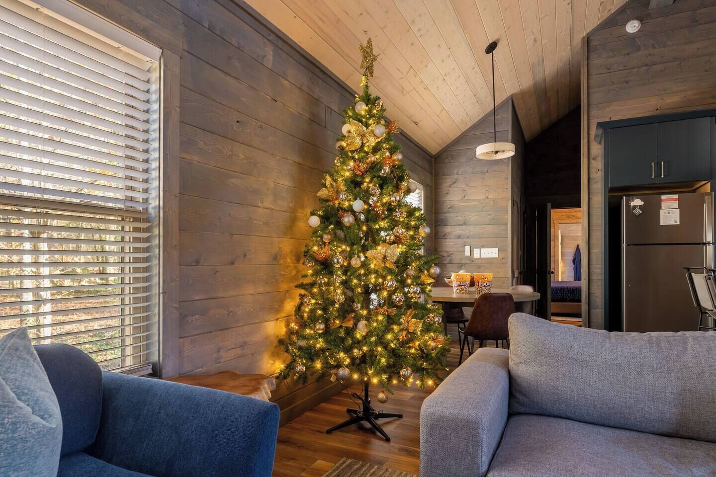 Ein gemütliches Wohnzimmer mit einem geschmückten Weihnachtsbaum, Holzwänden und einer modernen Küchenzeile.