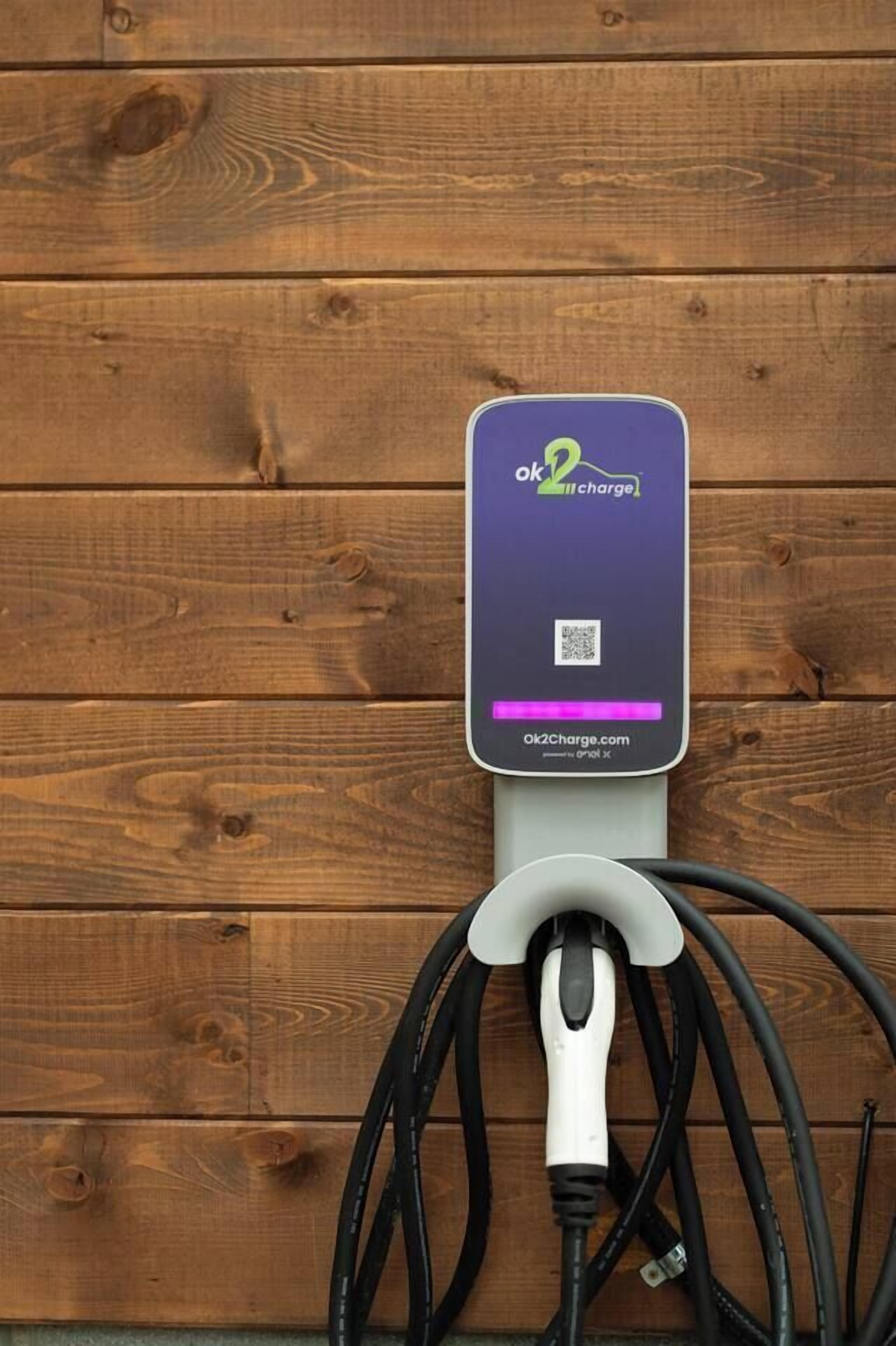An electric vehicle charging station with a purple and white charging unit, a QR code, and a cable connected to it.