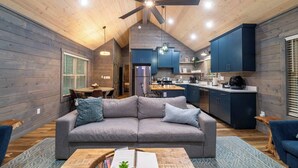 A modern interior with a gray sofa, wooden ceiling, and a kitchen area with blue cabinets. - Theater! Sauna! Jacuzzi! Firepit! EV Charger (Cosby)