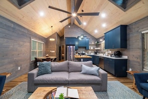 Ein modernes Interieur mit einem grauen Sofa, Holzboden und einer Küchenzeile mit blauen Schränken.