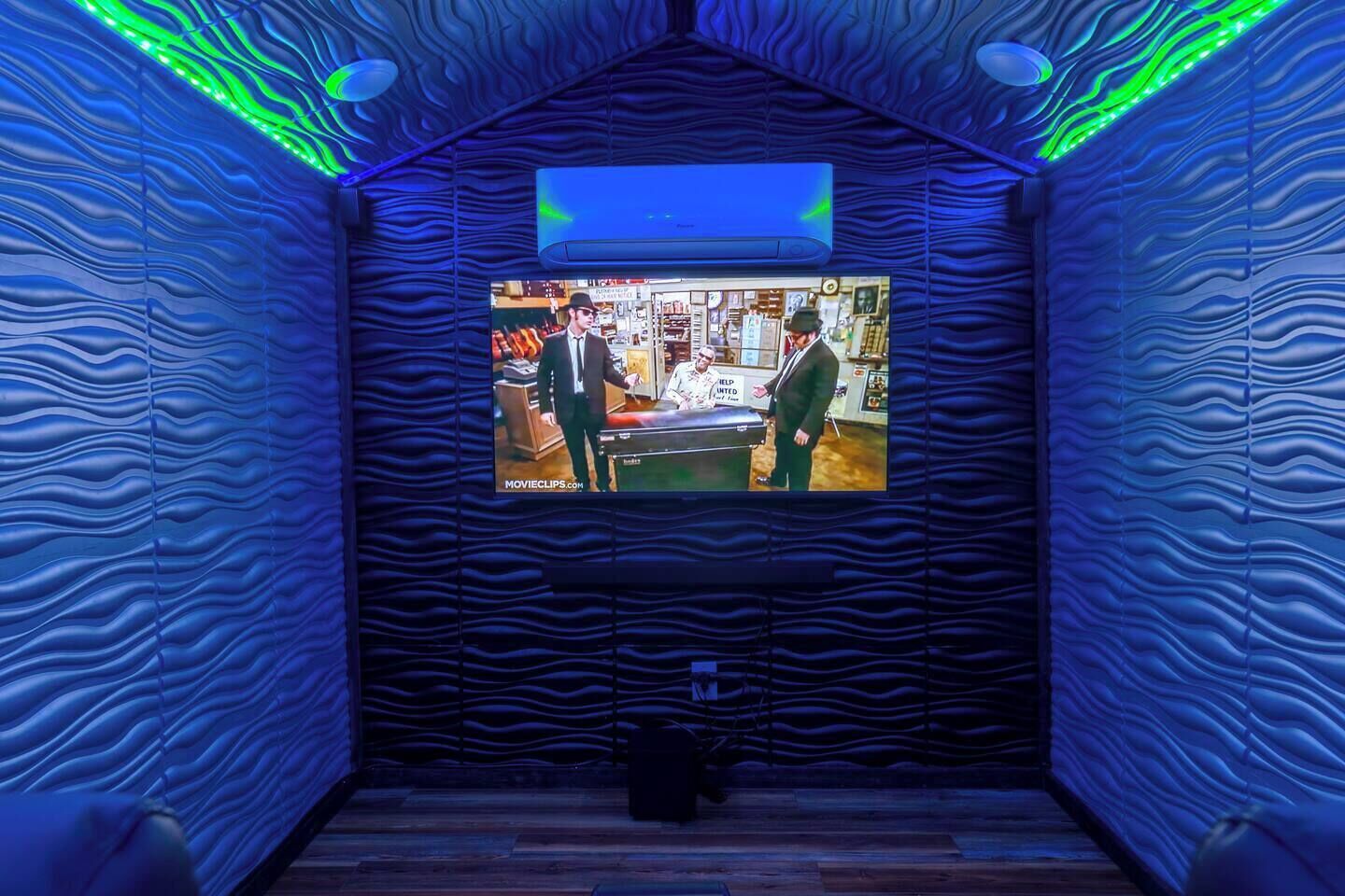 Ein Zimmer mit an der Wand befestigtem Fernseher, Holzboden und einer Decke mit wellenförmigem Muster.