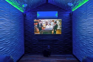 A room with a television mounted on a textured wall, a wooden floor, and a ceiling with a wavy design. - Theater! Sauna! Jacuzzi! Firepit! EV Charger (Cosby)