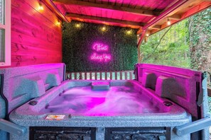 A hot tub with a neon sign, surrounded by wooden walls and a green wall with foliage. - Theater! Sauna! Jacuzzi! Firepit! EV Charger (Cosby)