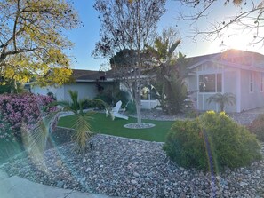 Una propiedad residencial con un césped cuidado, un patio con mobiliario exterior y una variedad de plantas y árboles.