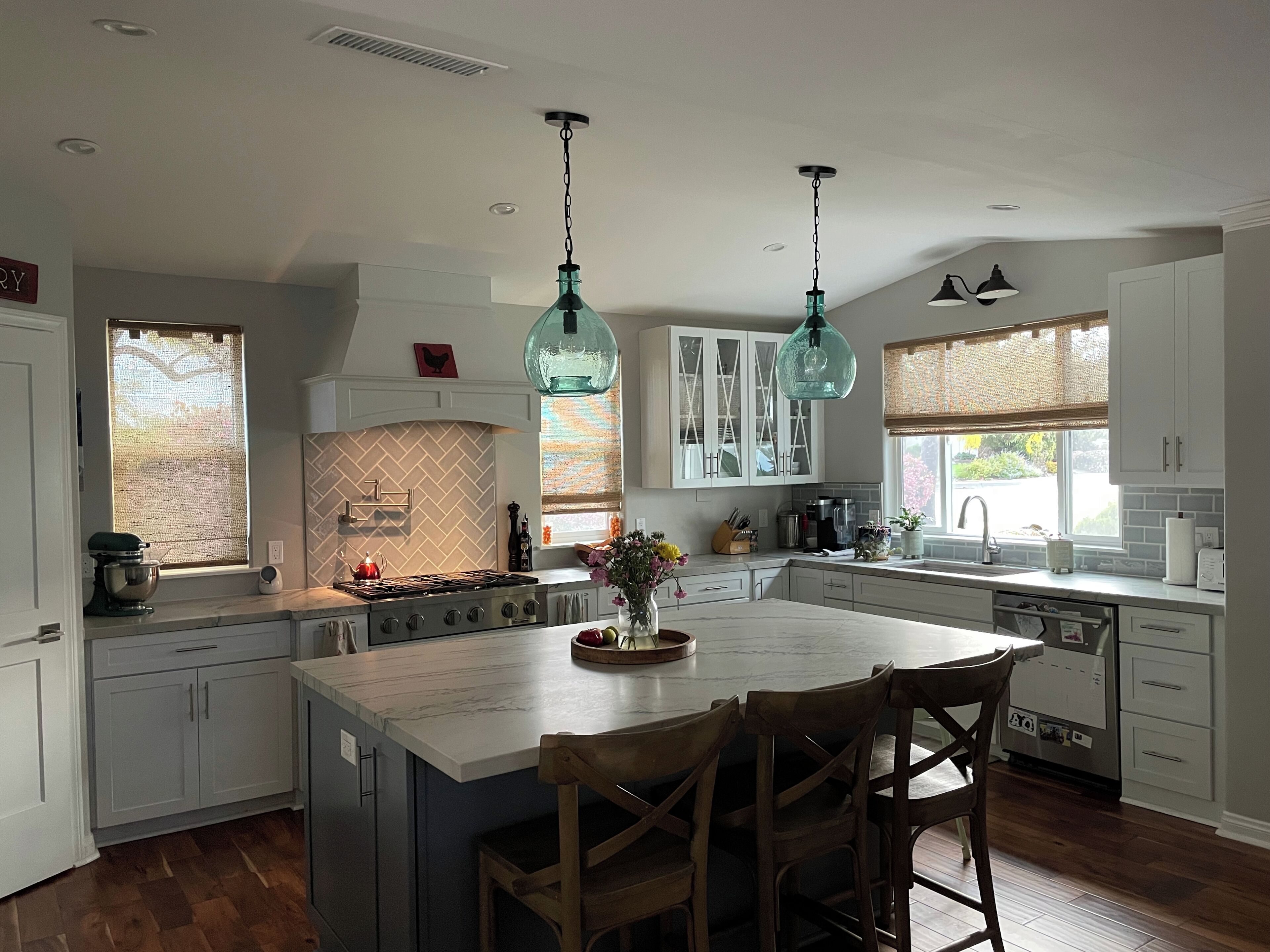 A kitchen with white cabinets, a central island, wooden chairs, and pendant lighting.