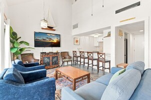 A living room with a large TV, a sailboat decoration, and a dining area with wooden chairs.