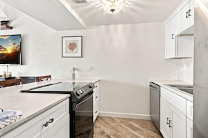 A modern kitchen with white cabinetry, a stainless steel range, and a wooden floor. - Sand Dollar W-210 (Pensacola Beach)