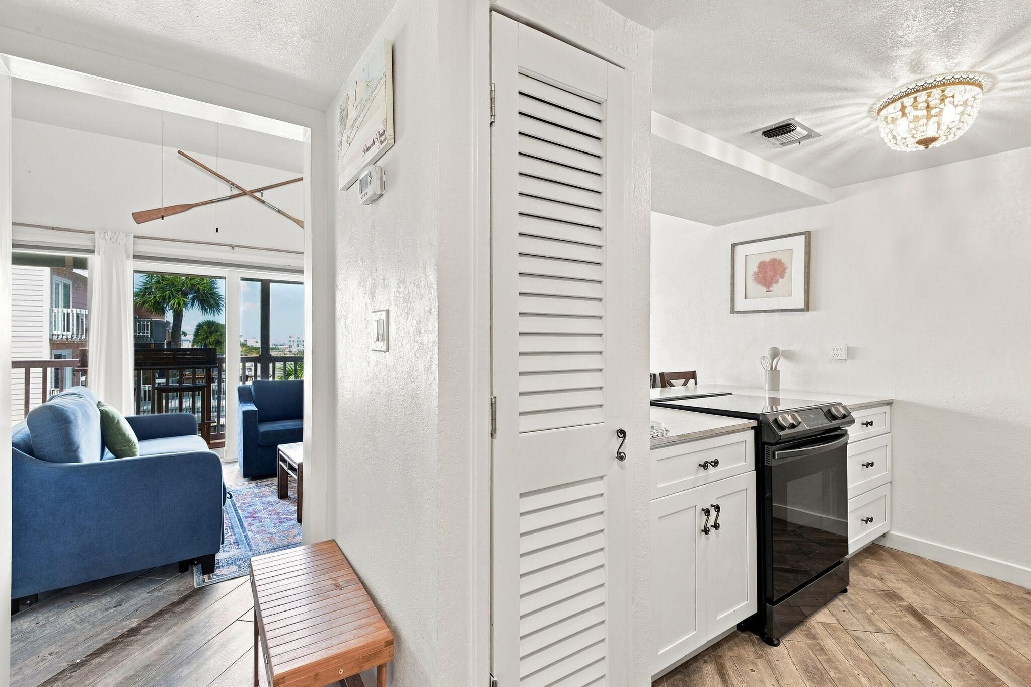 A modern kitchen with white cabinetry, a built-in oven, and a dining area with a blue sofa and a wooden bench.