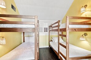 A bunk bed room with wooden frames, white bedding, and wall-mounted lamps. - Sand Dollar W-210 (Pensacola Beach)