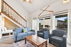 A spacious living room with a wooden staircase, a large sofa set, and a view to the outside. - Sand Dollar W-210 (Pensacola Beach)
