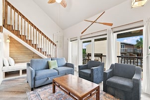 A spacious living room with a wooden staircase, a large sofa set, and a view to the outside.