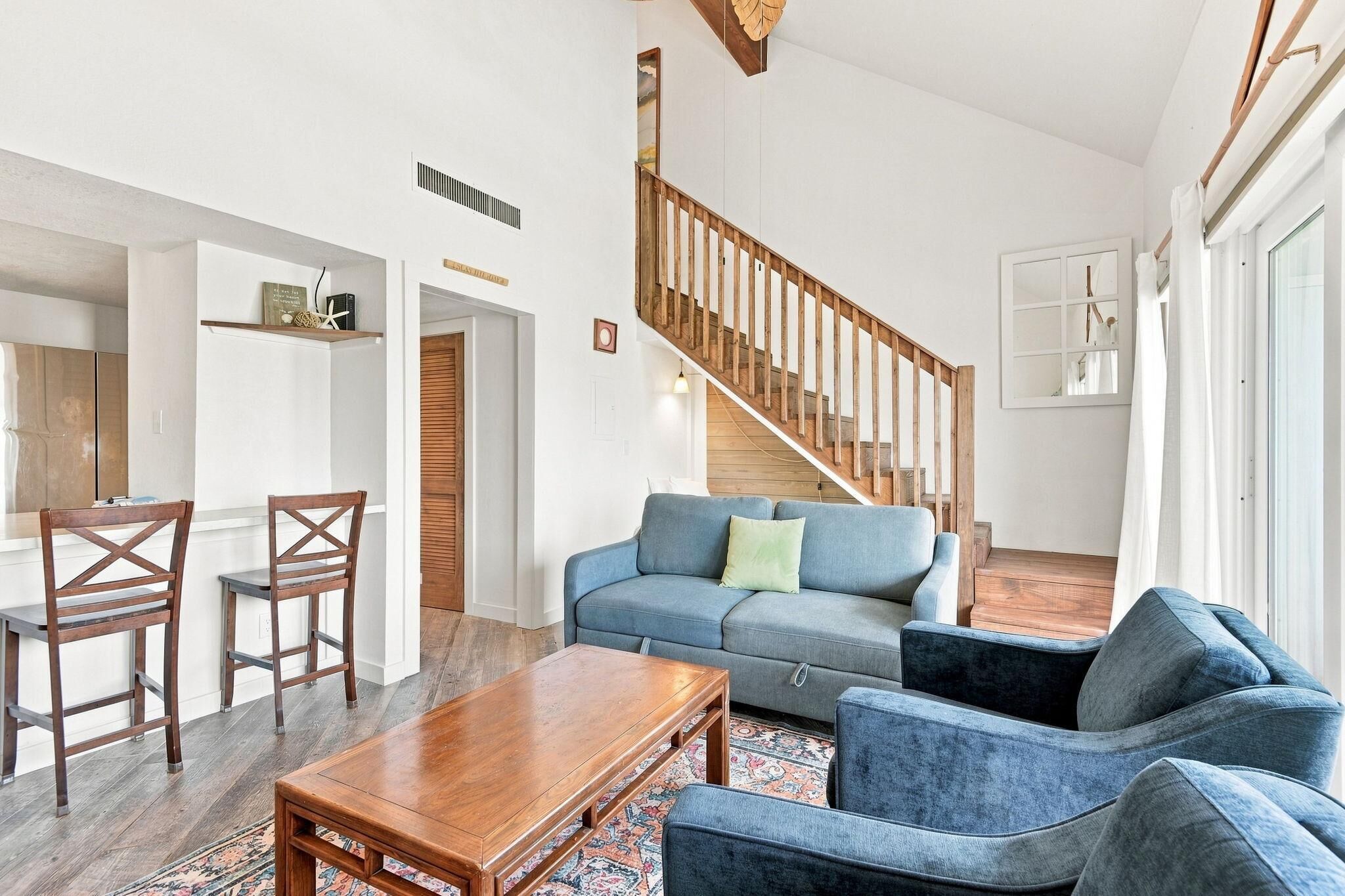 A spacious living area with a wooden staircase, a blue sofa, a wooden coffee table, and a patterned rug.